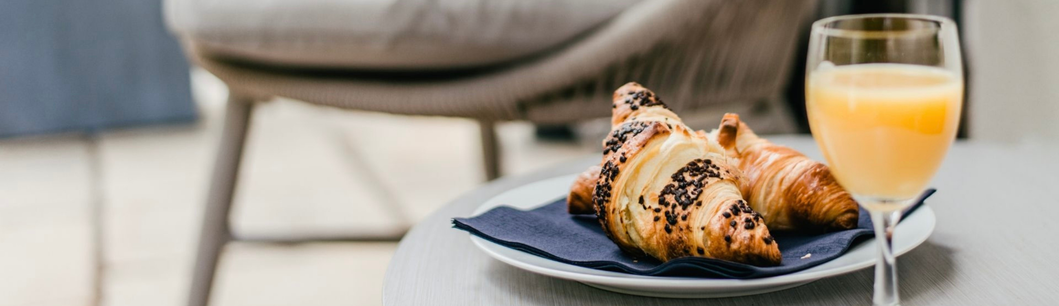 Zwei Croissants auf einem Teller mit Serviette und einem Glas Orangensaft