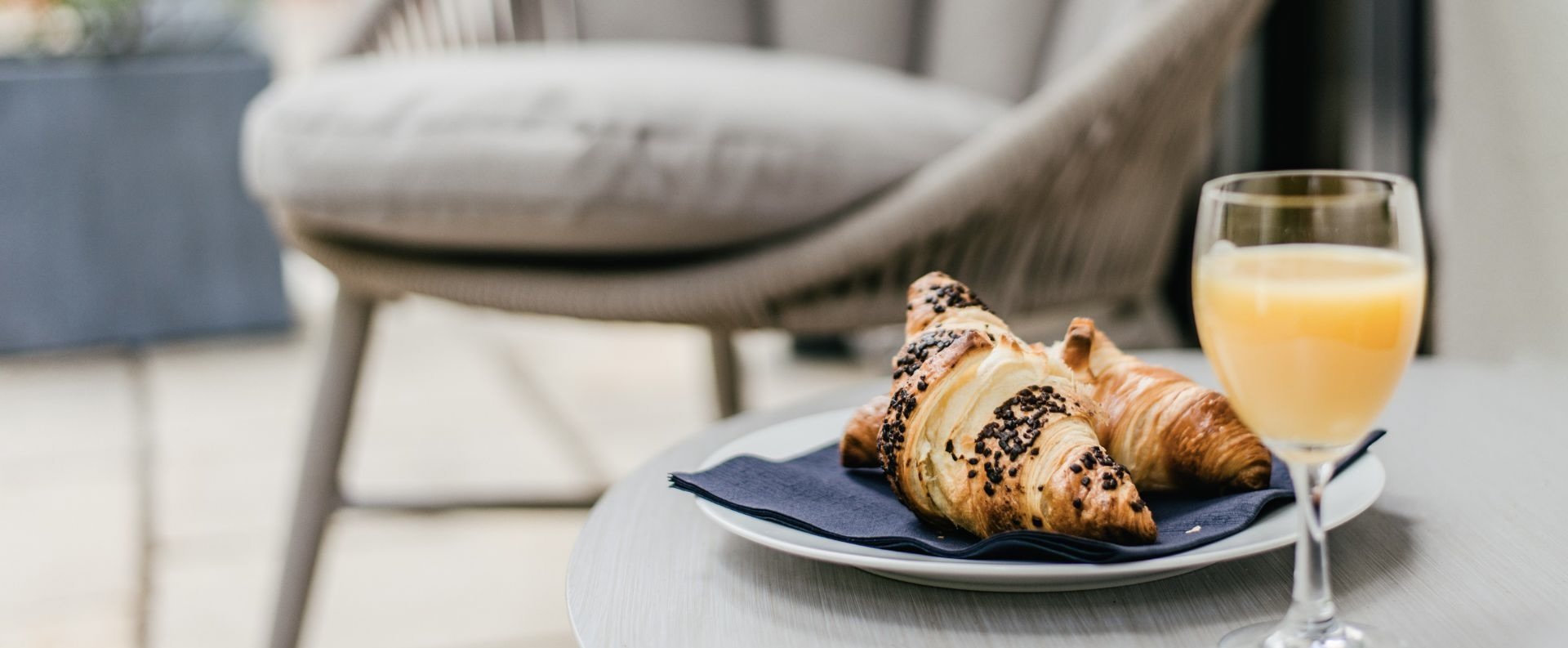 Zwei Croissants auf einer blauen Serviette auf einem Teller mit einem Glas Orangensaft im Vordergrund